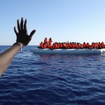 Migrants on a rubber boat gesture as they are rescued by SOS Mediterranee organisation in the Mediterranean Sea