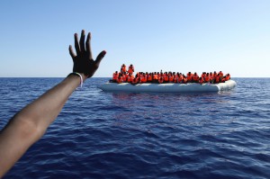 Migrants on a rubber boat gesture as they are rescued by SOS Mediterranee organisation in the Mediterranean Sea